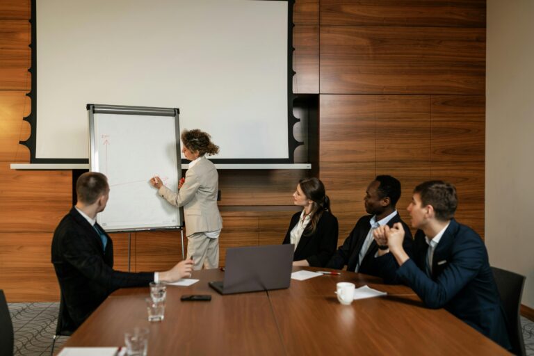 Colleagues sitting at a conference room while a workshop facilitator introduces a topic on a whiteboard.